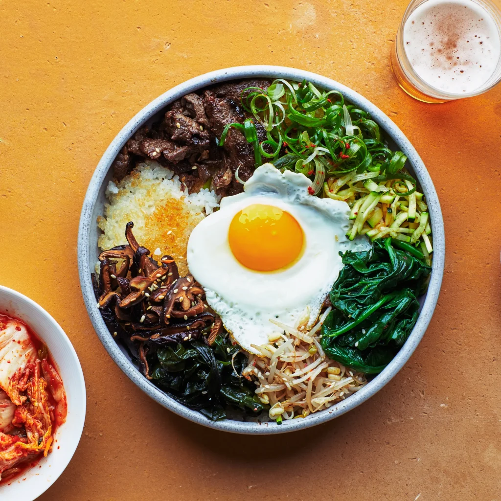 a bowl of traditional Korean bibimbap served on a yellow table with kimchi on the side