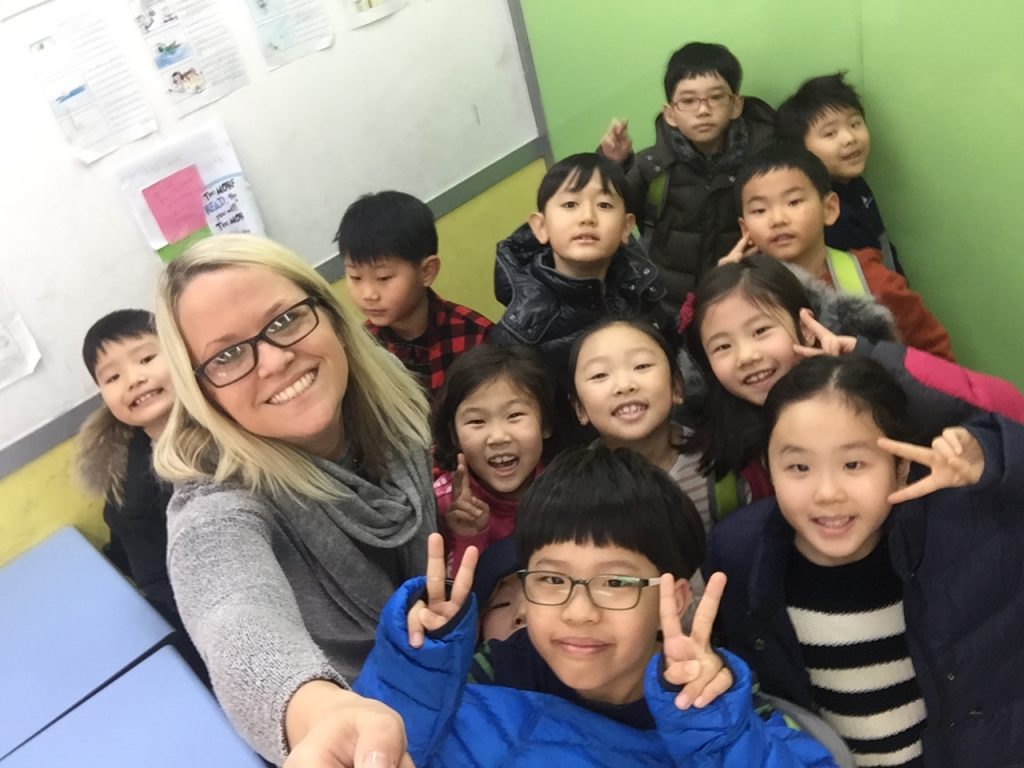 A foreign English language teacher posing with selfie stick with her students in a Chungdahm Learning classroom in Korea