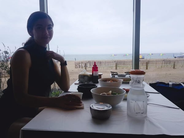 woman posing at a restaurant table with an ocean view in background