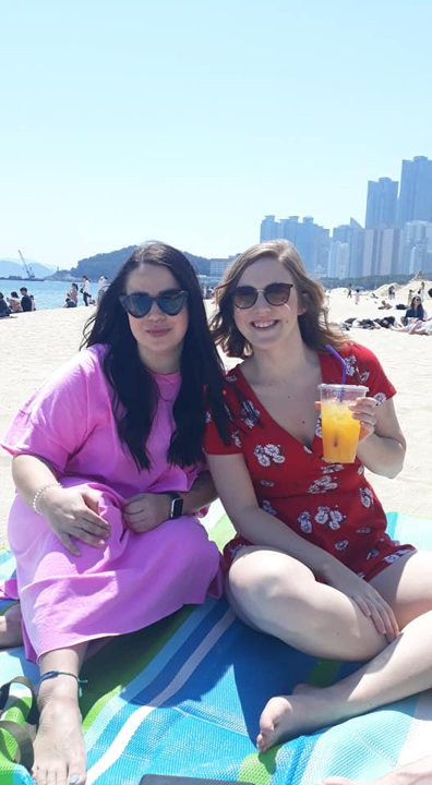 two women holding a drink on the beach in busan highlighting life in korea