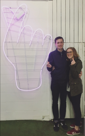 Couple posing in front of a neon sign with a hand making the heart gesture in Korea
