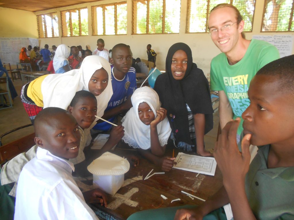 A peace Corps volunteer posing with students working on a project in a classroom in Tanzania, Africa