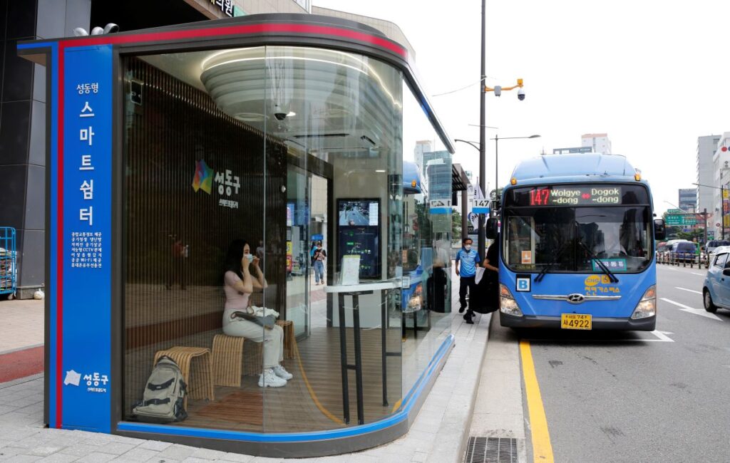 Woman waits for a bus inside a glass-covered bus stop in Seoul, Korea.