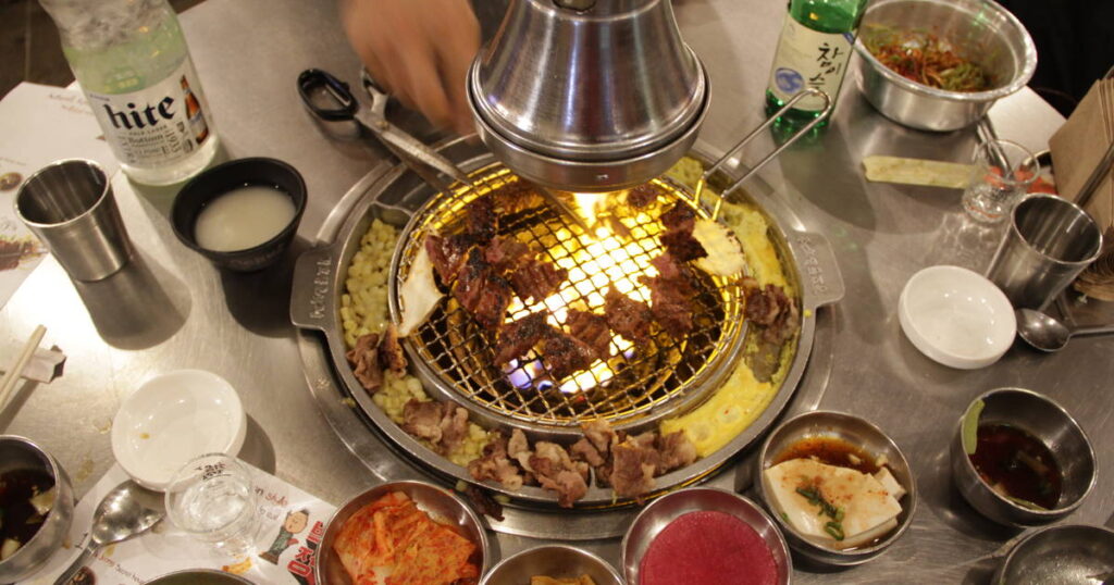 A Korean BBQ table with pork cooking on hot coals.